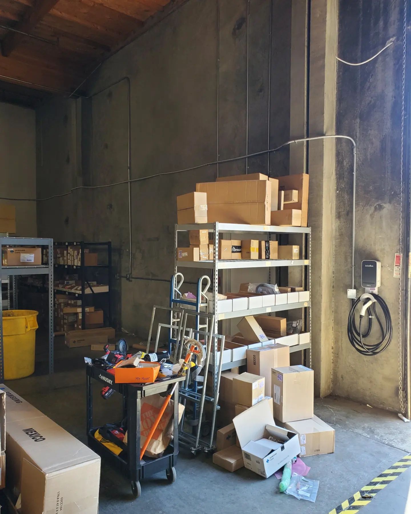 Warehouse interior with shelving, boxes, tools on cart, and an open doorway.