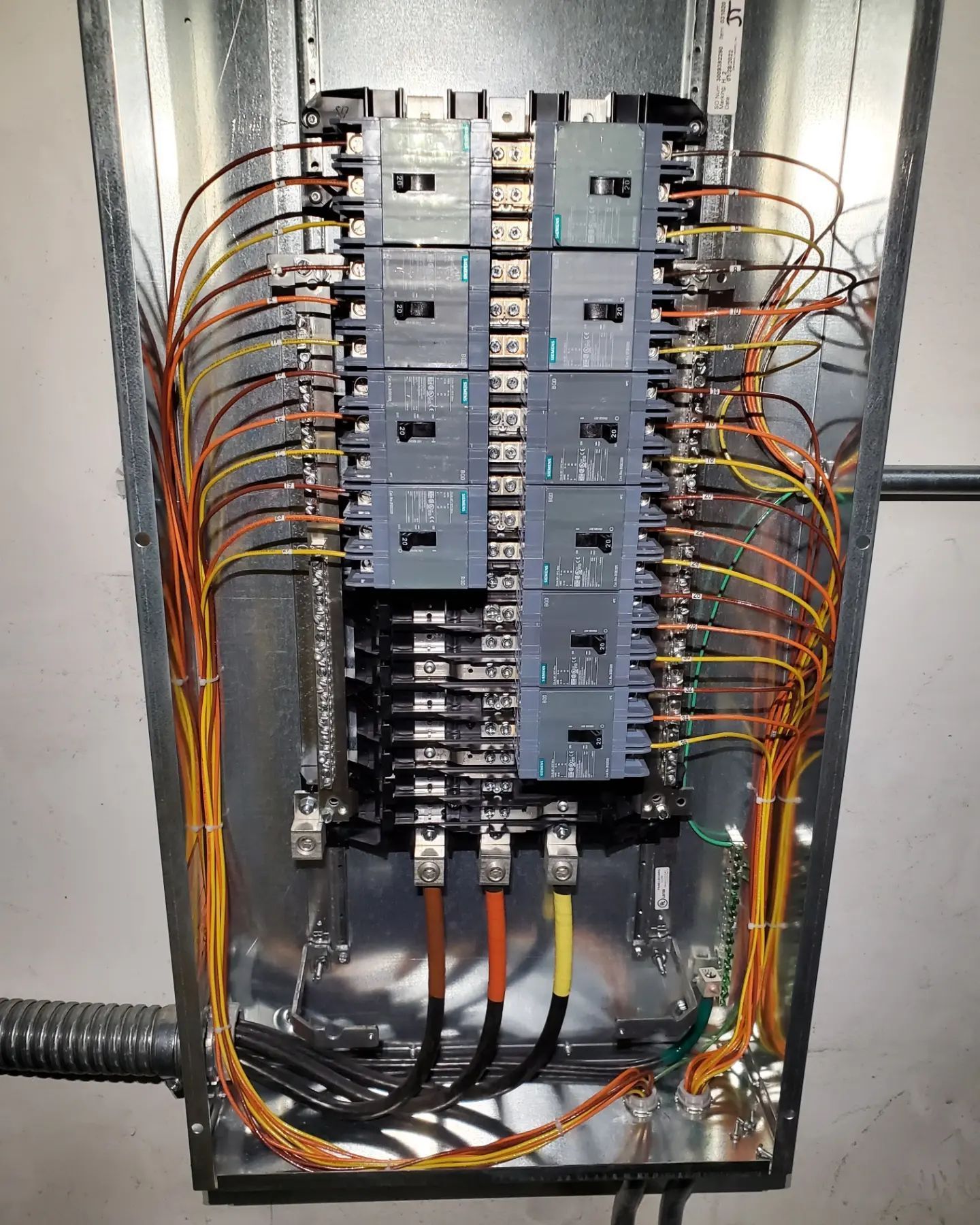Electrical panel with circuit breakers and color-coded wires in a metal enclosure.