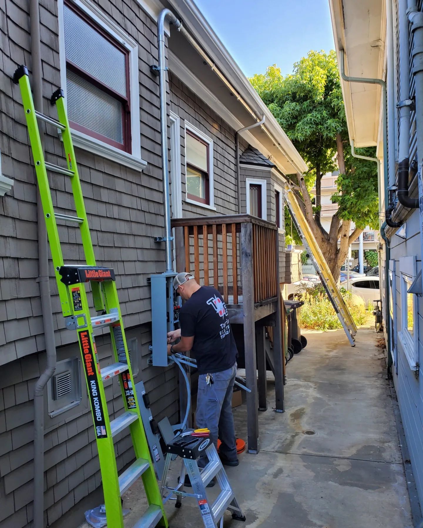 Electrician works on a breaker box on the side of a building, using a ladder.