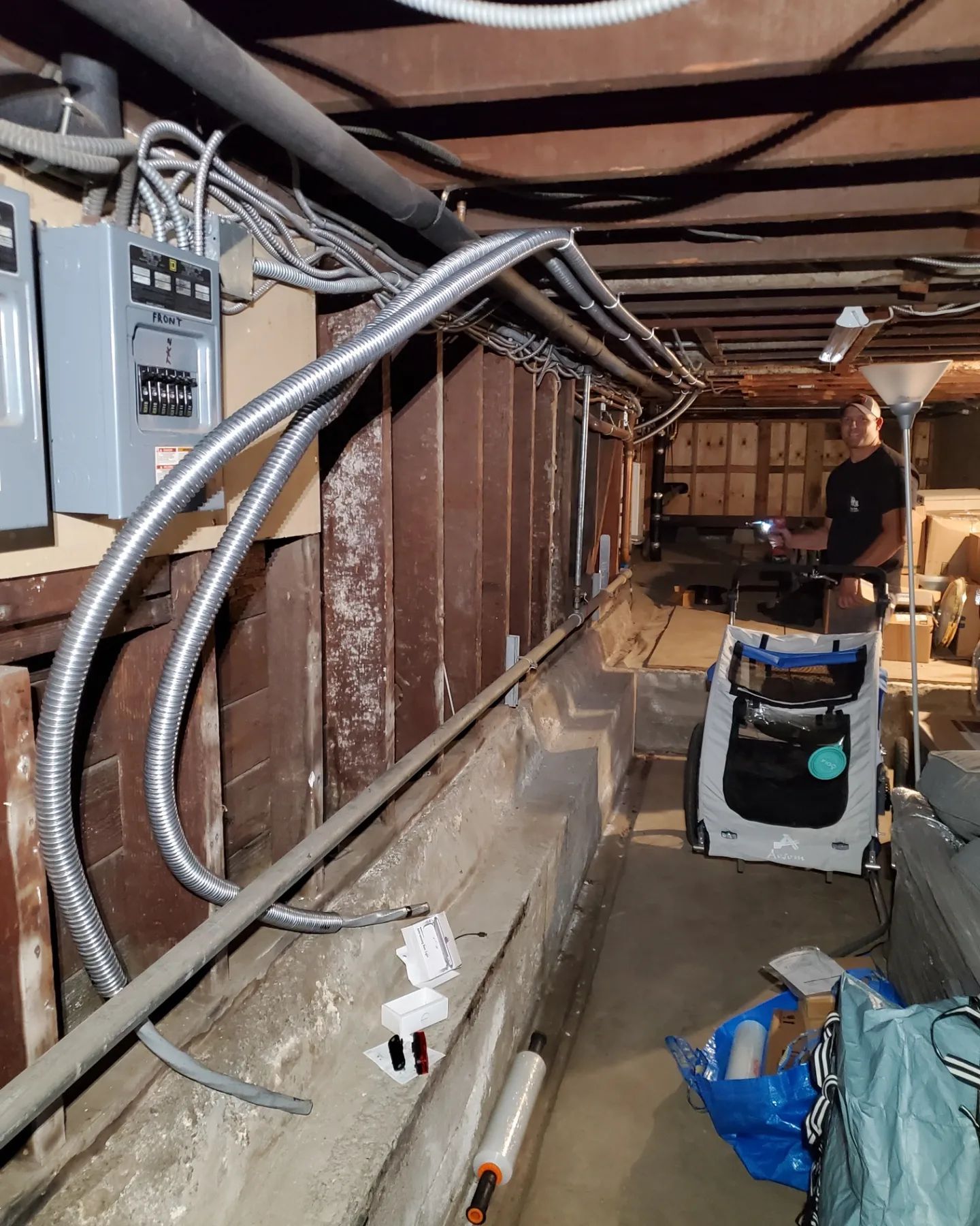 Electrical wiring in a basement. Person standing, holding a device. Silver flexible conduit, grey breaker box.