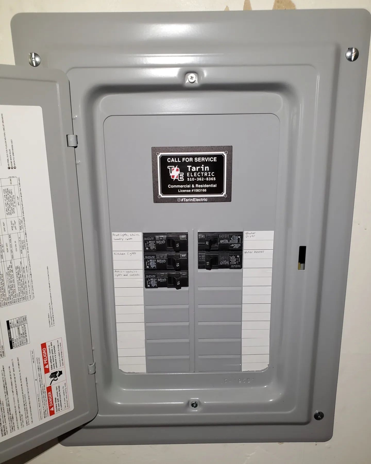 Gray electrical panel with open door, showing circuit breakers and labeling.