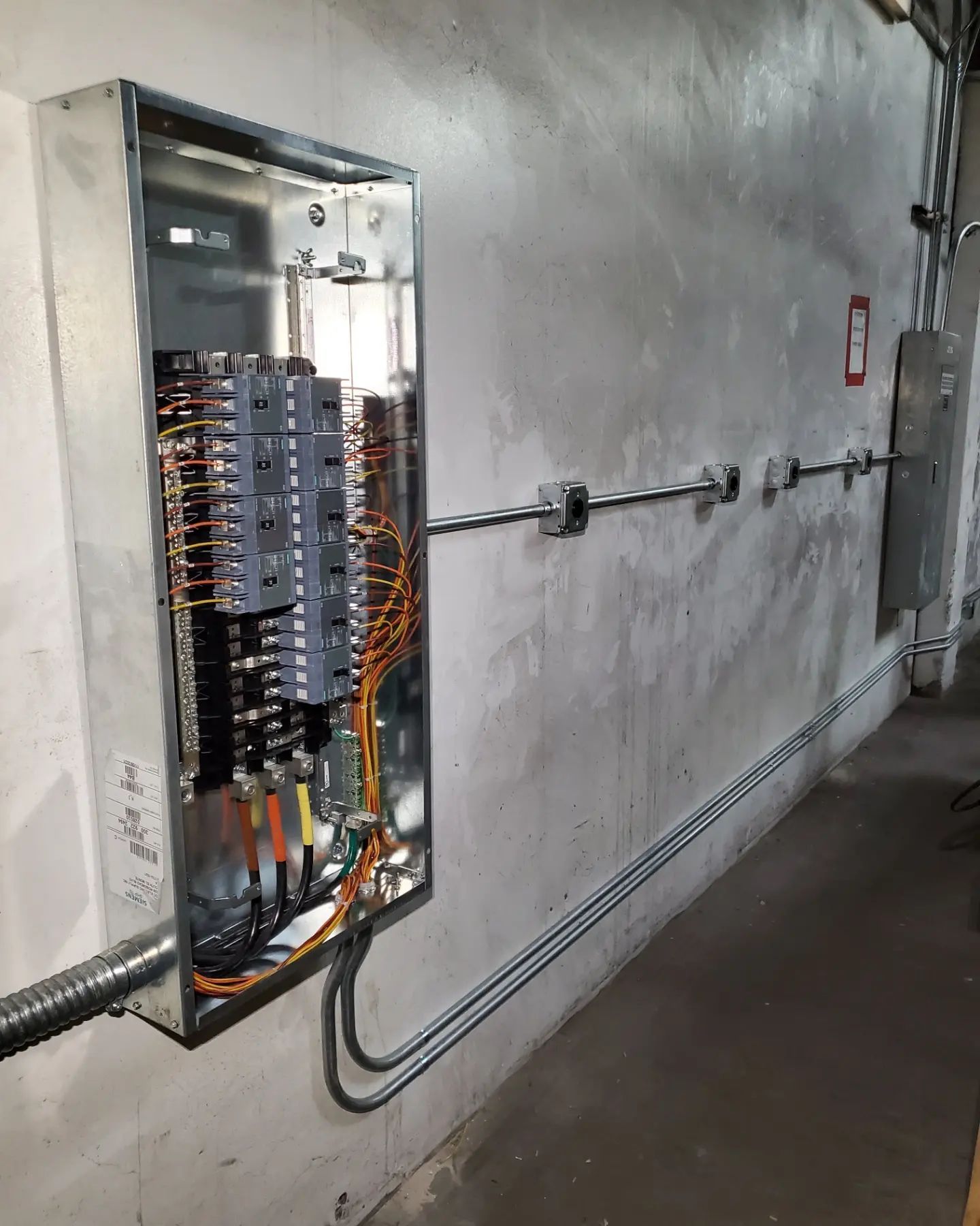 Electrical panel mounted on a concrete wall with conduit running along the wall.