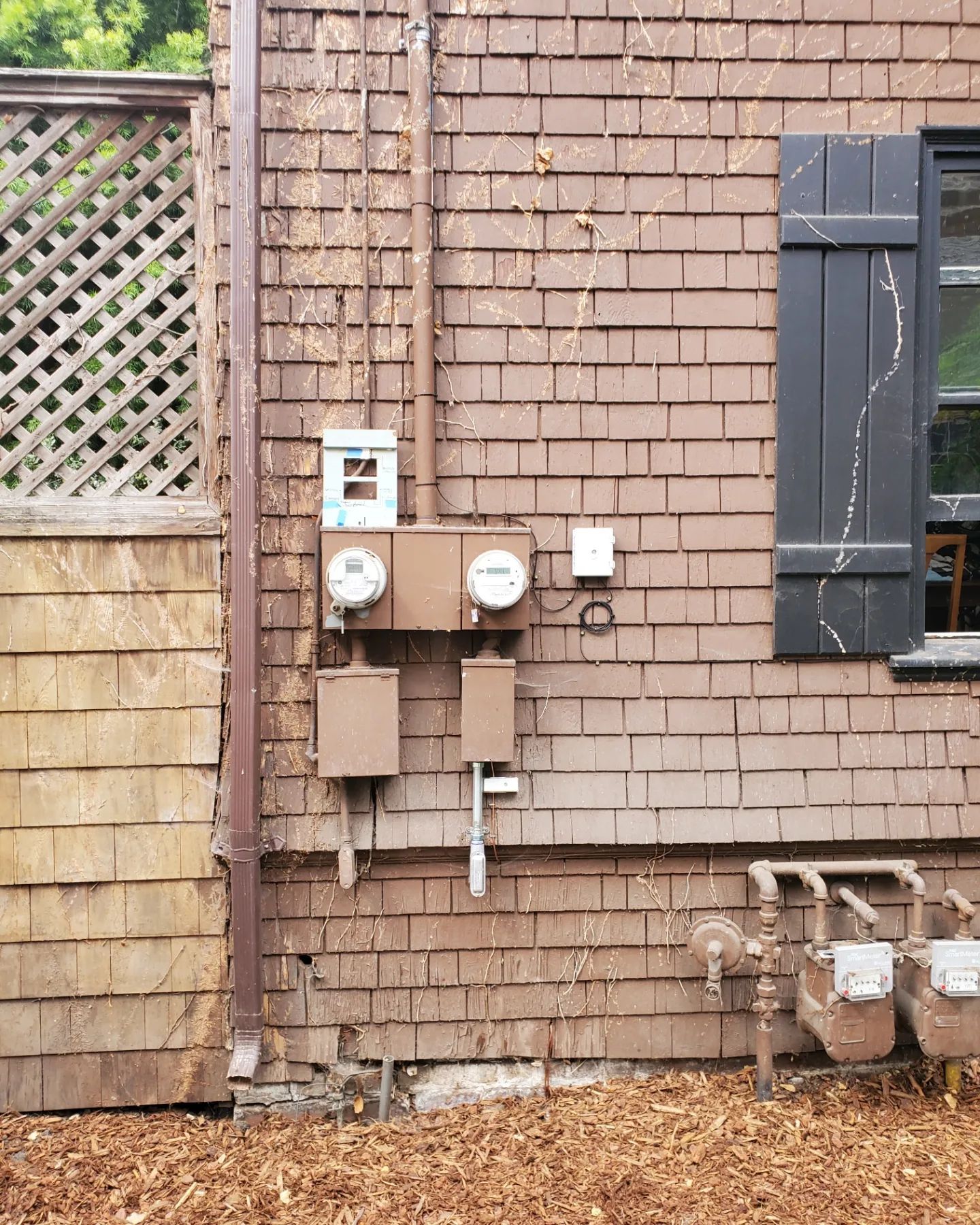 Brown building exterior with electrical meters, pipes, and a shuttered window.