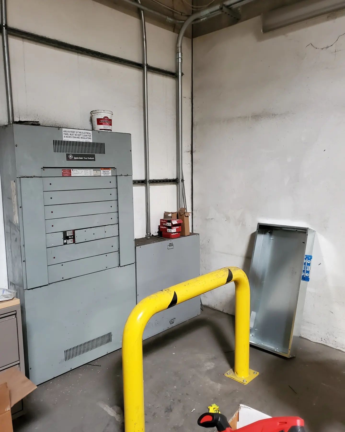 Electrical panel in a room, with yellow protective barrier. Conduit runs along the wall.