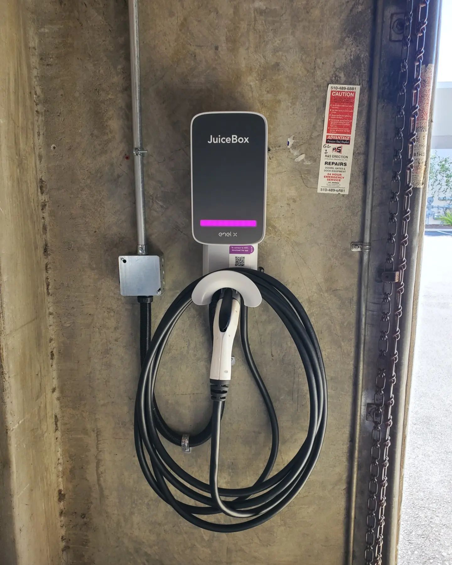 Electric vehicle charger mounted on a concrete wall; black cable coiled below the charger.
