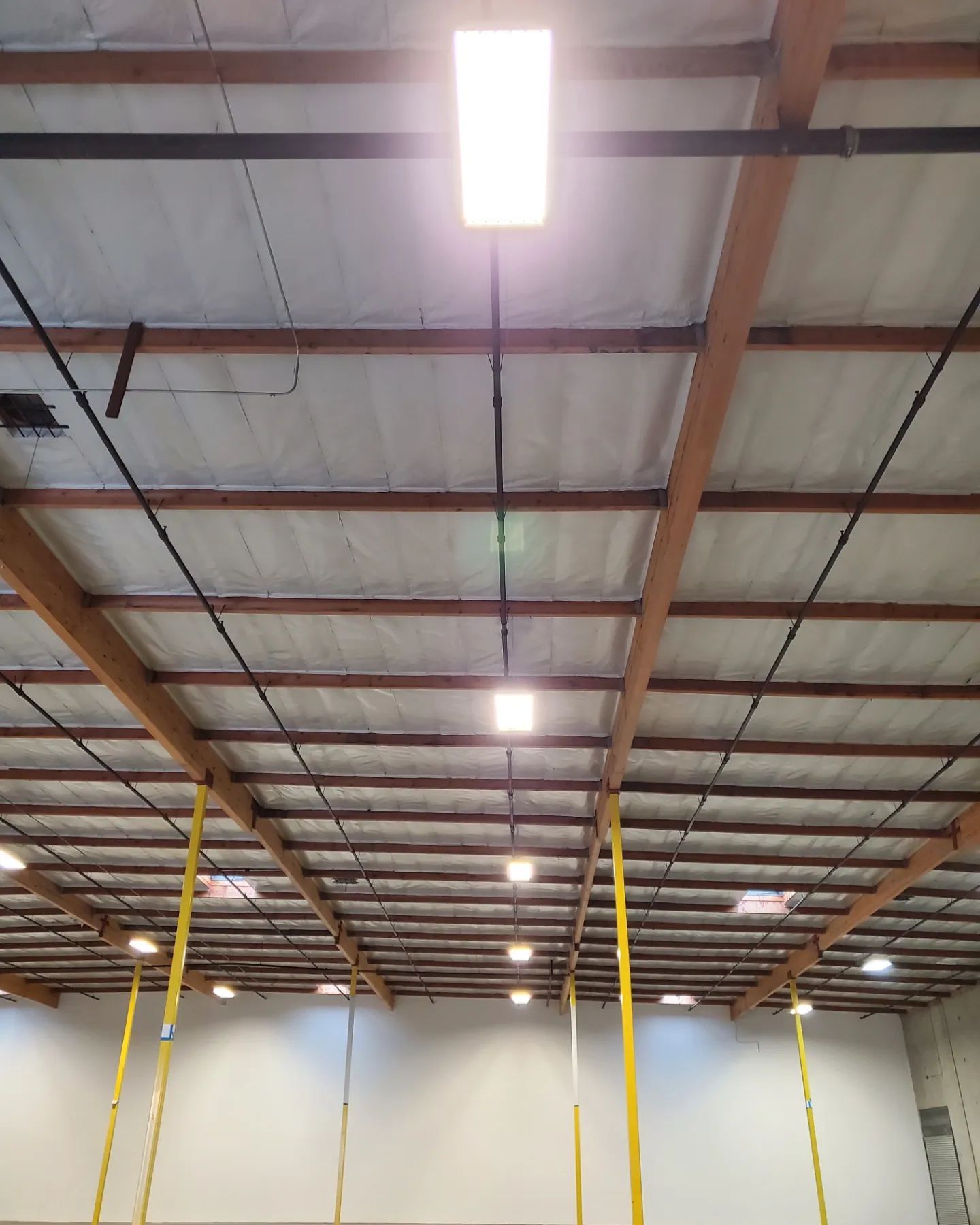 Warehouse ceiling with bright overhead lights and exposed wooden beams.