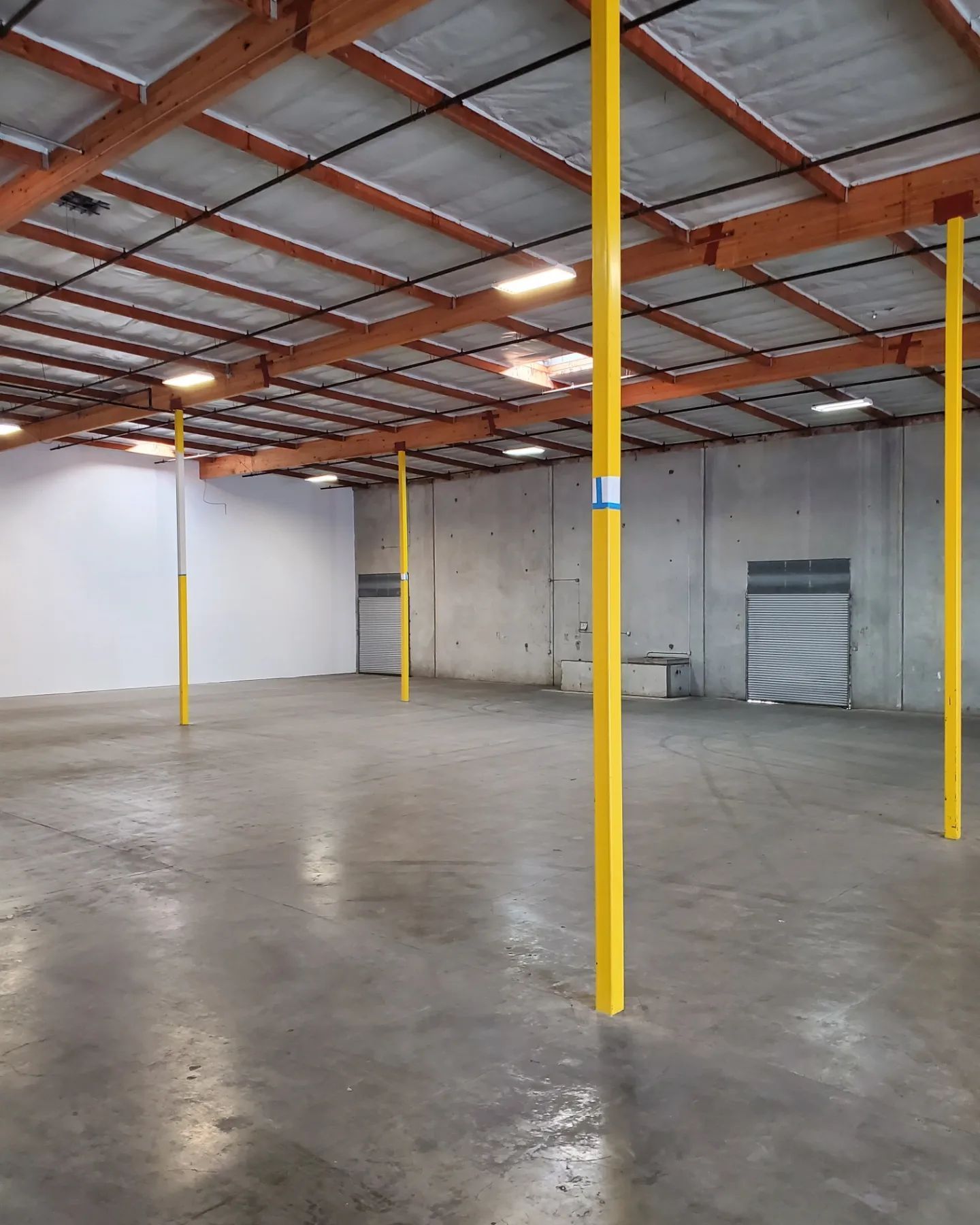 Empty warehouse with yellow support beams and concrete floor.