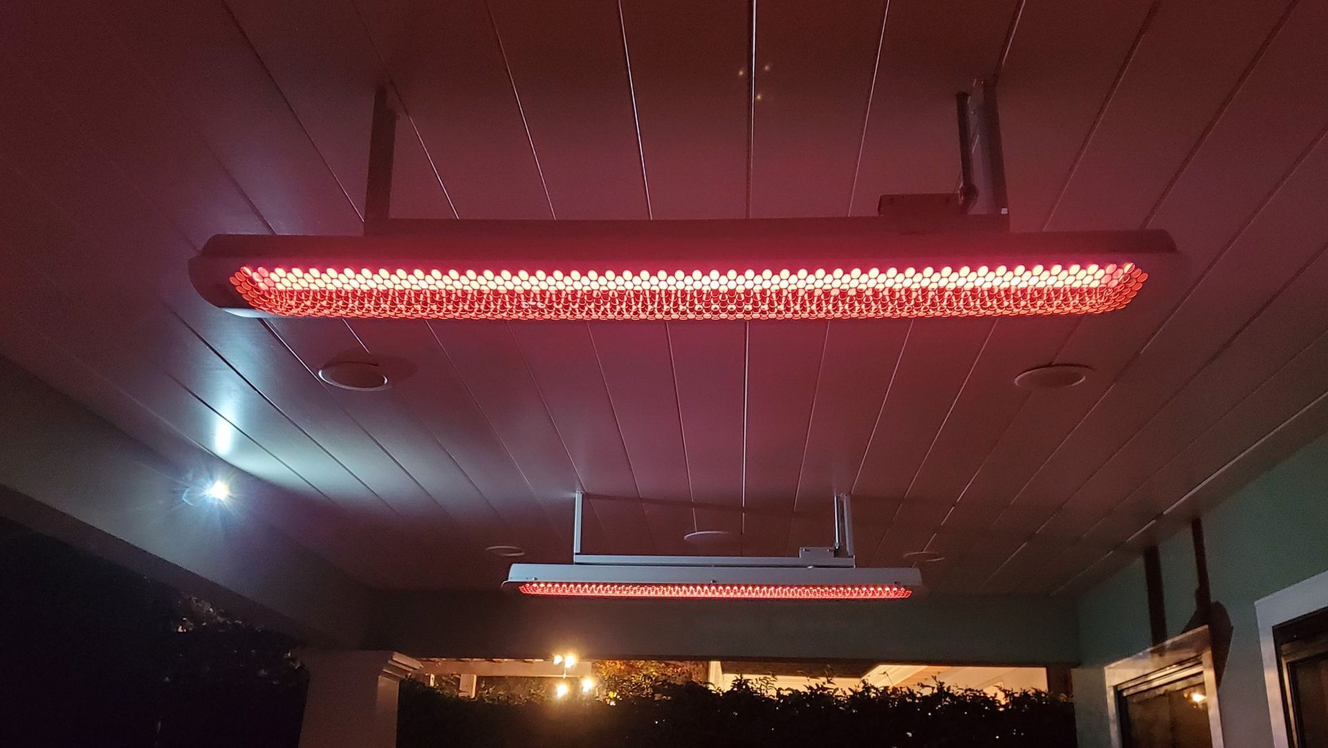 Two red infrared heaters hanging from a wooden ceiling, illuminating the area below.
