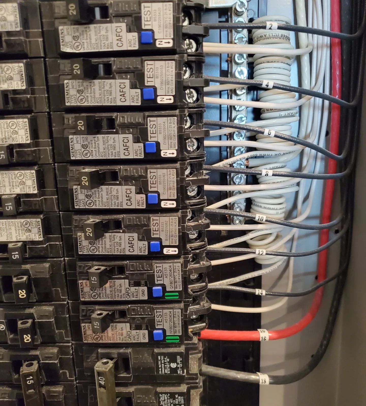 Electrical circuit breaker panel with labeled breakers and wires.