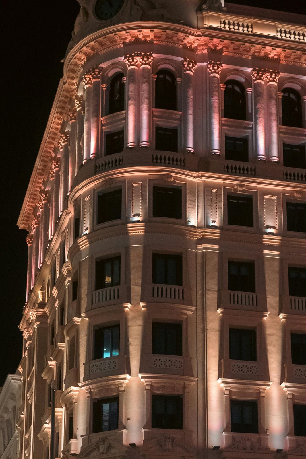 Illuminated ornate building at night, with multiple floors and columns, bathed in warm and cool lighting.