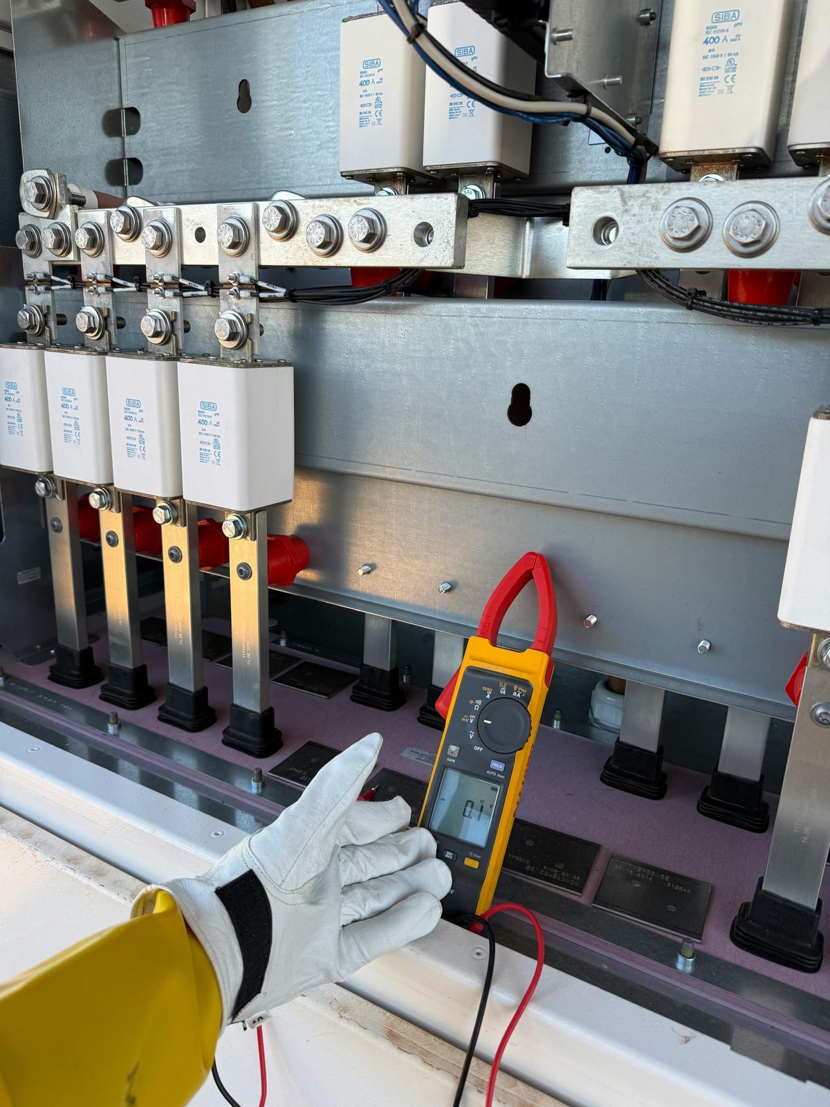 Hand with glove using clamp meter on electrical components.