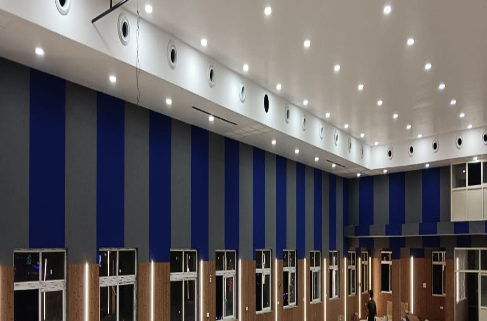 Interior view of a large room with blue and gray striped walls, windows, and numerous ceiling lights.