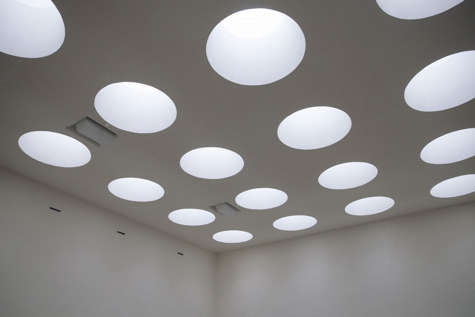 Ceiling with many circular, bright skylights, casting light into a white-walled room.