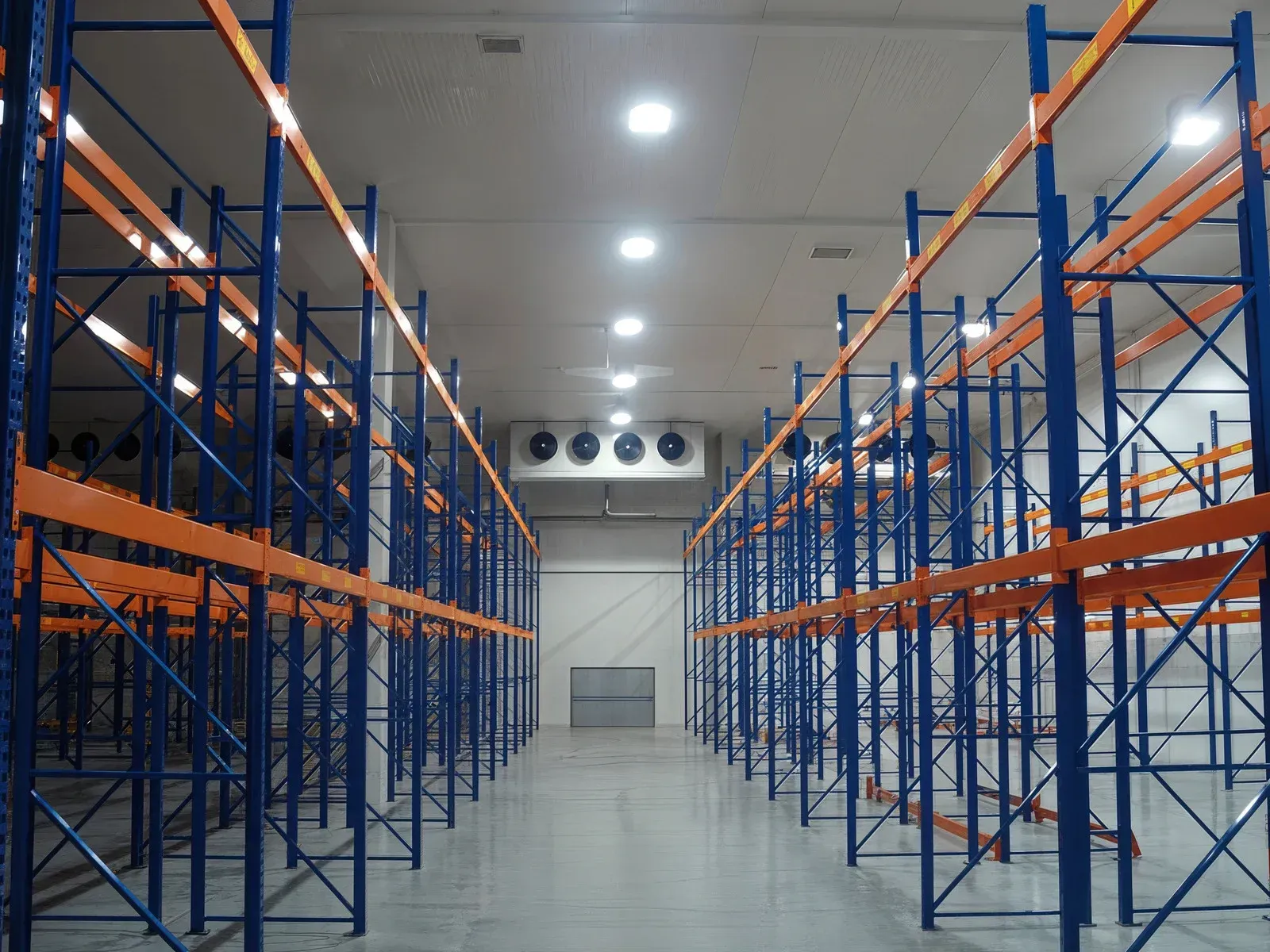 Empty warehouse interior with blue shelving, orange beams, and overhead lighting.