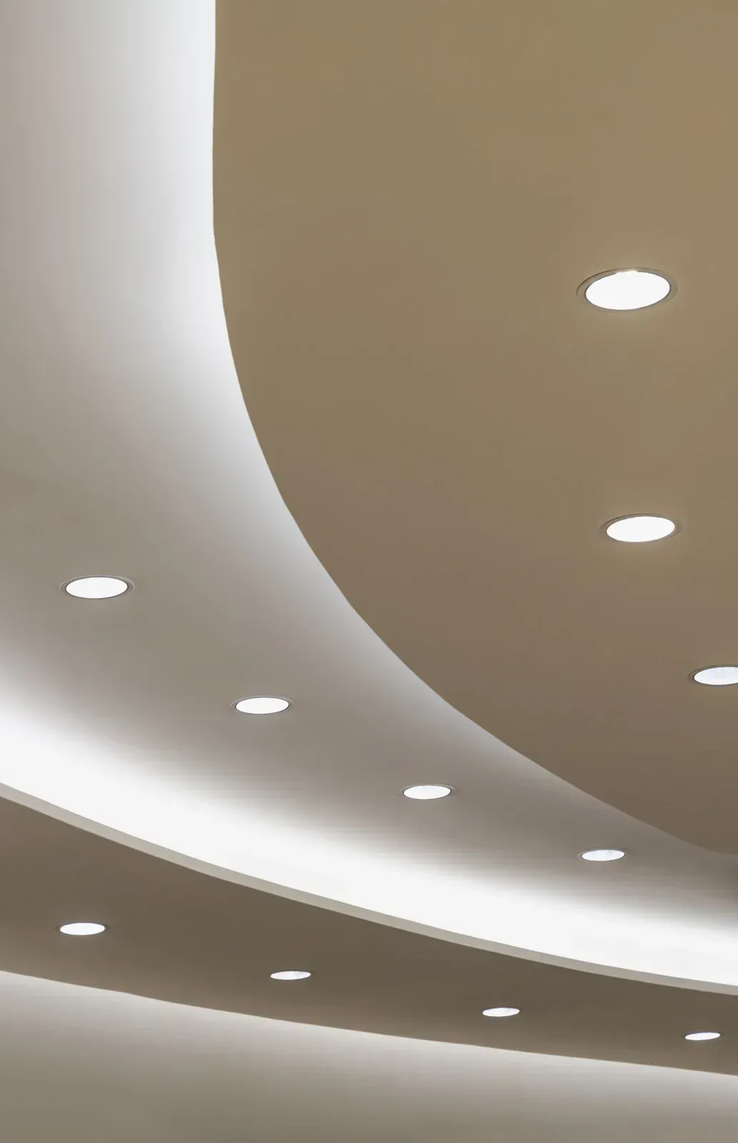 Curved ceiling with recessed lights and a glowing cove light. Beige and white.