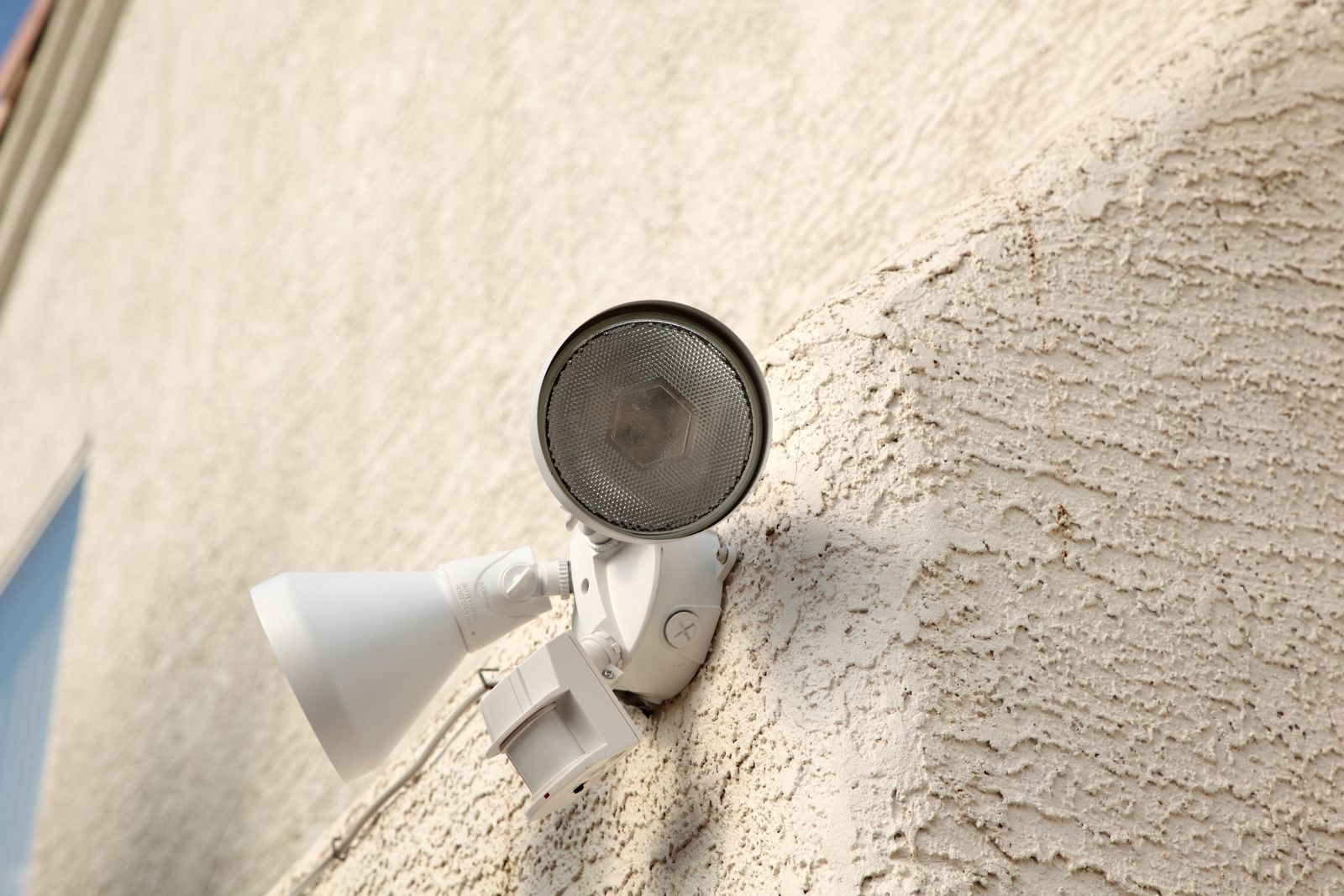 White security light fixture attached to a stucco wall.