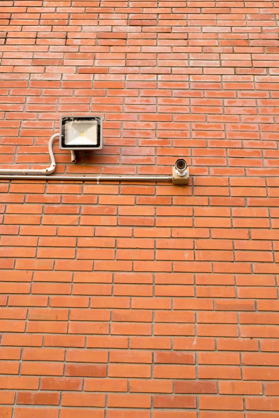 Red brick wall with a security light and a pipe.