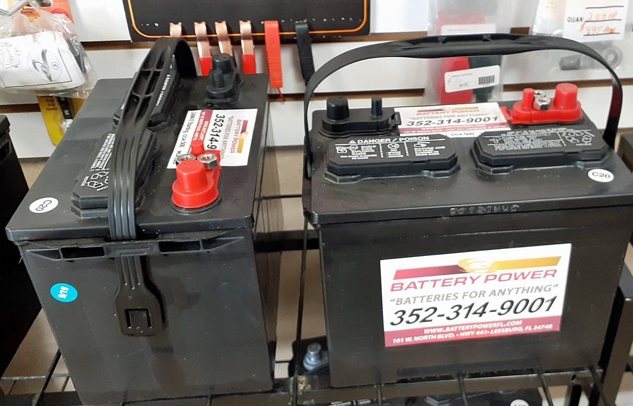 Two black car batteries with red and black terminals on display in a store.