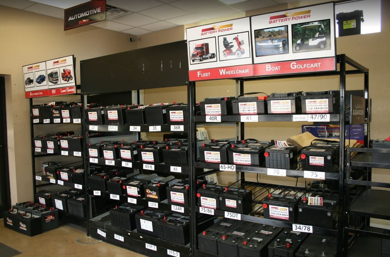 Shelves filled with car batteries in a store; signs display uses like RV, boat, and golf cart.