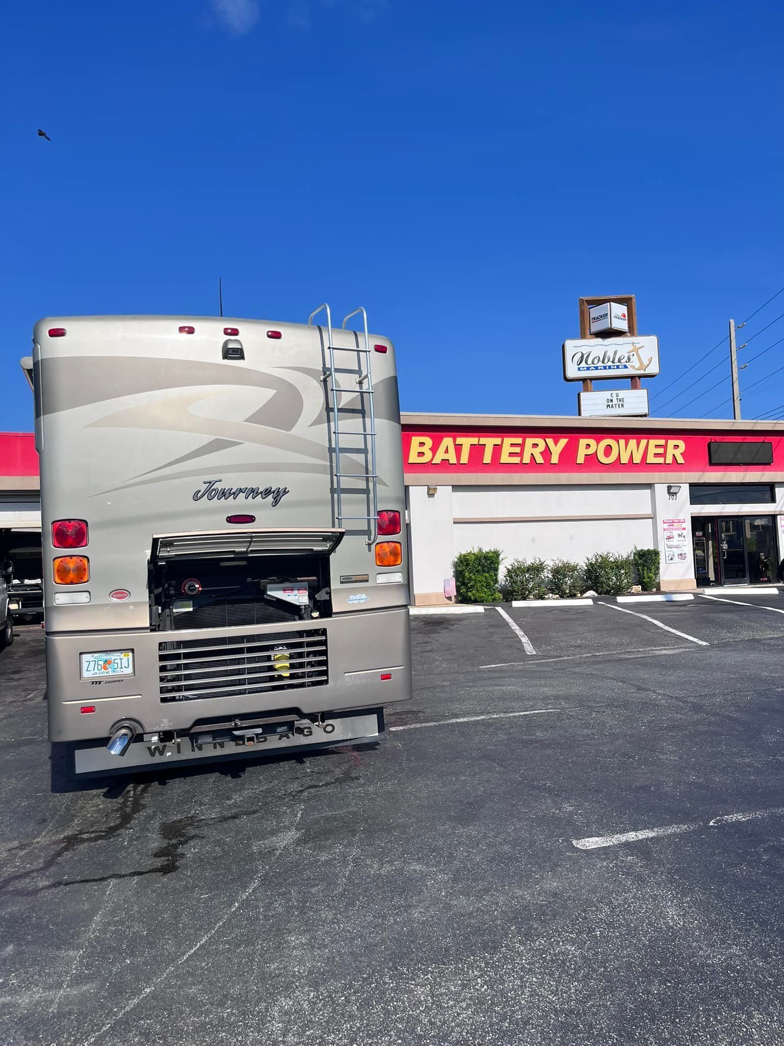 RV parked at Battery Power store, rear view; tan and silver, blue sky.