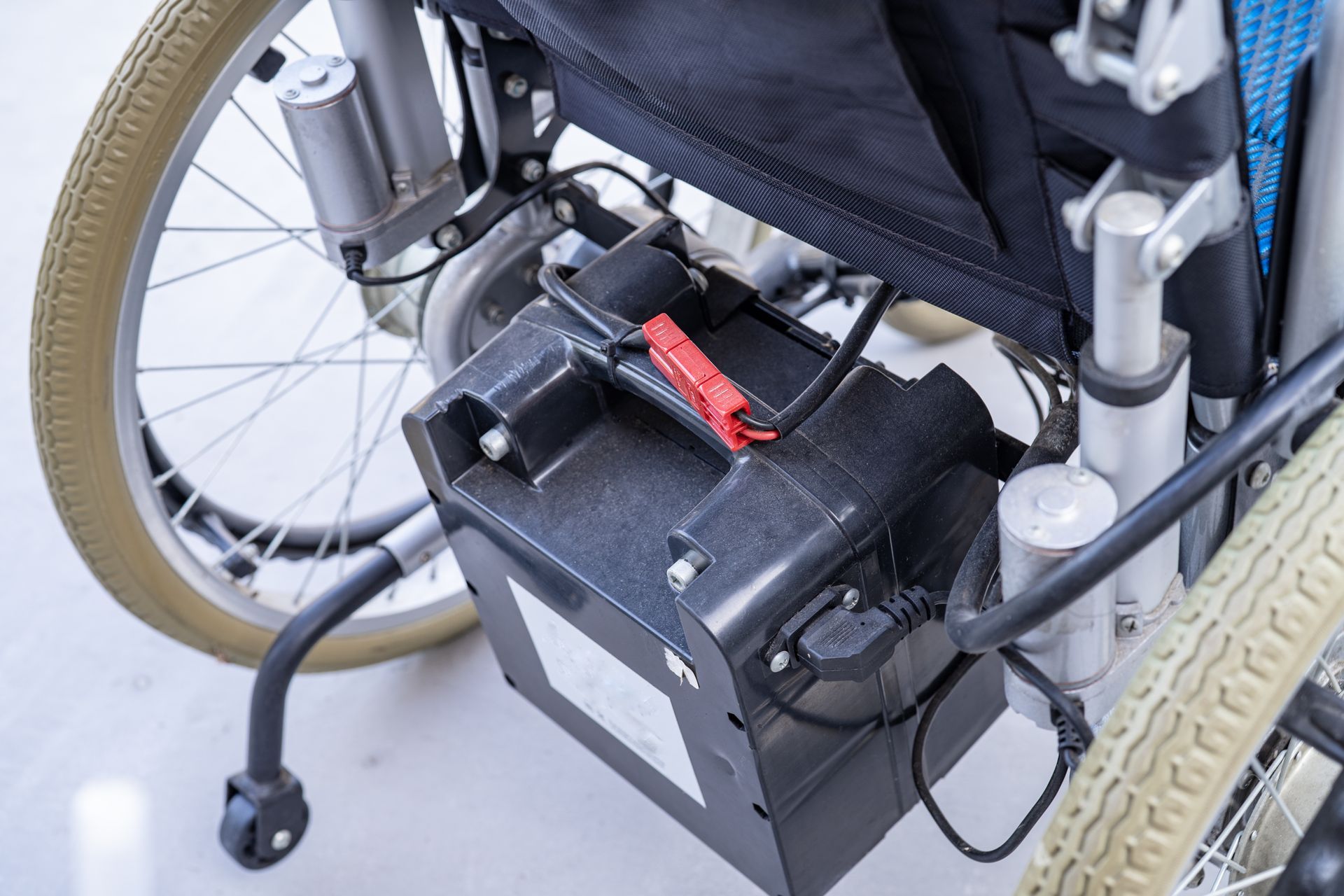 Battery and motor on a motorized wheelchair, shown from the side. Black battery, beige tires, and blue seat.
