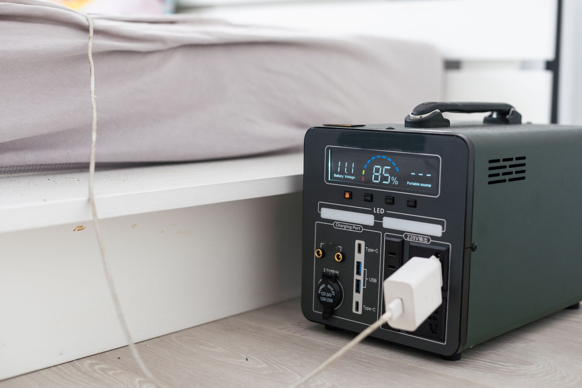 A black portable power station on the floor near a bed with a white plug inserted, showing a battery charge of 95%.