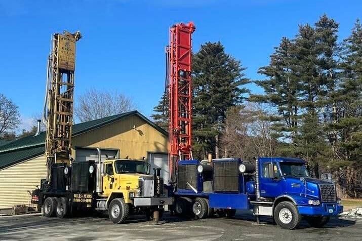 Two well drilling trucks are parked next to each other in front of a building.