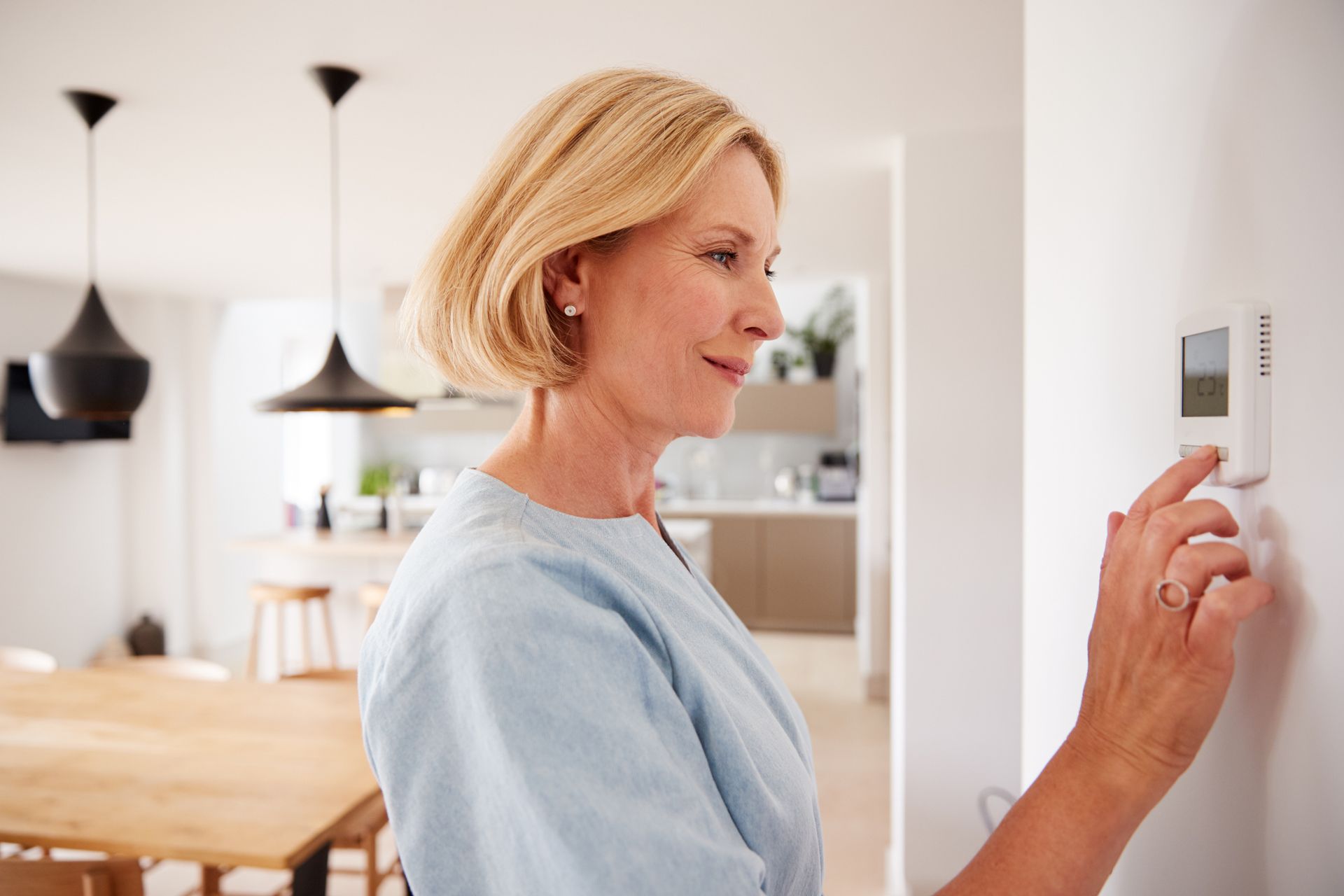 A woman is adjusting a thermostat in a living room.