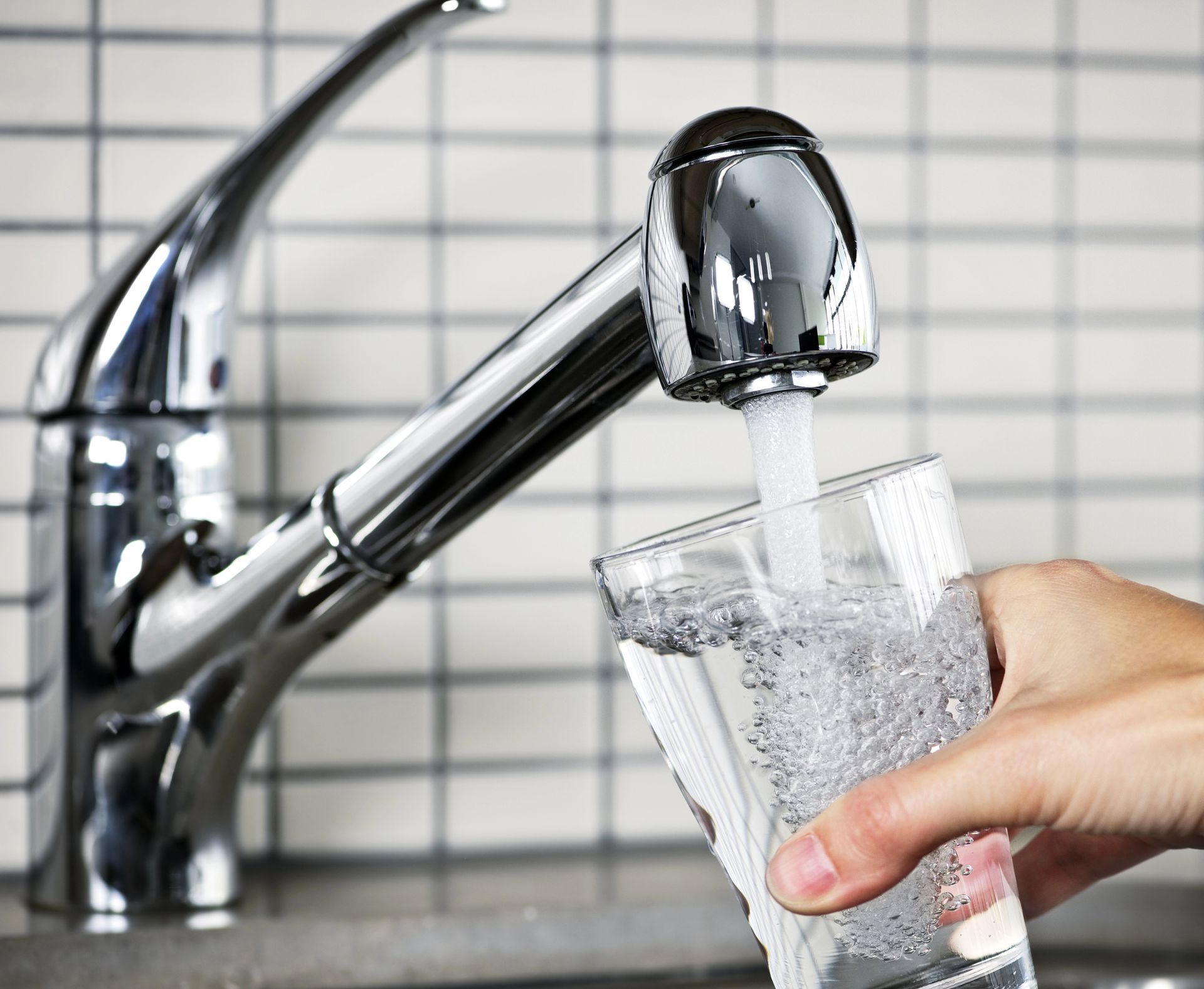 A person is pouring water from a faucet into a glass