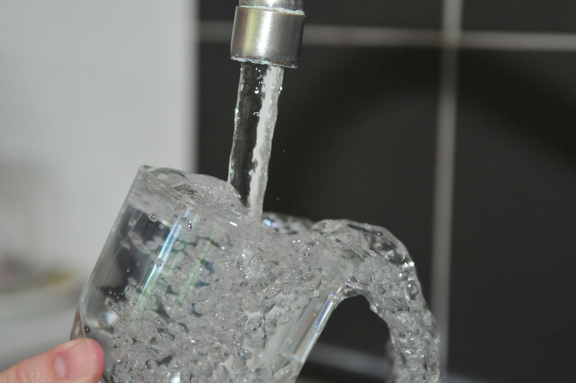 A person is holding a glass of water under a faucet.