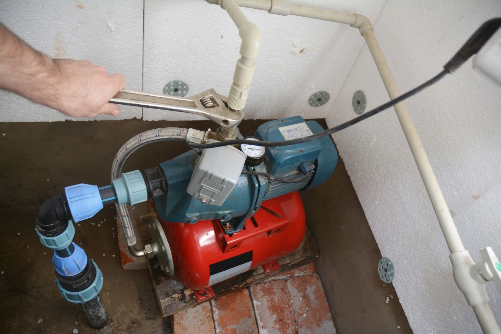 A person is working on a water pump with a wrench.