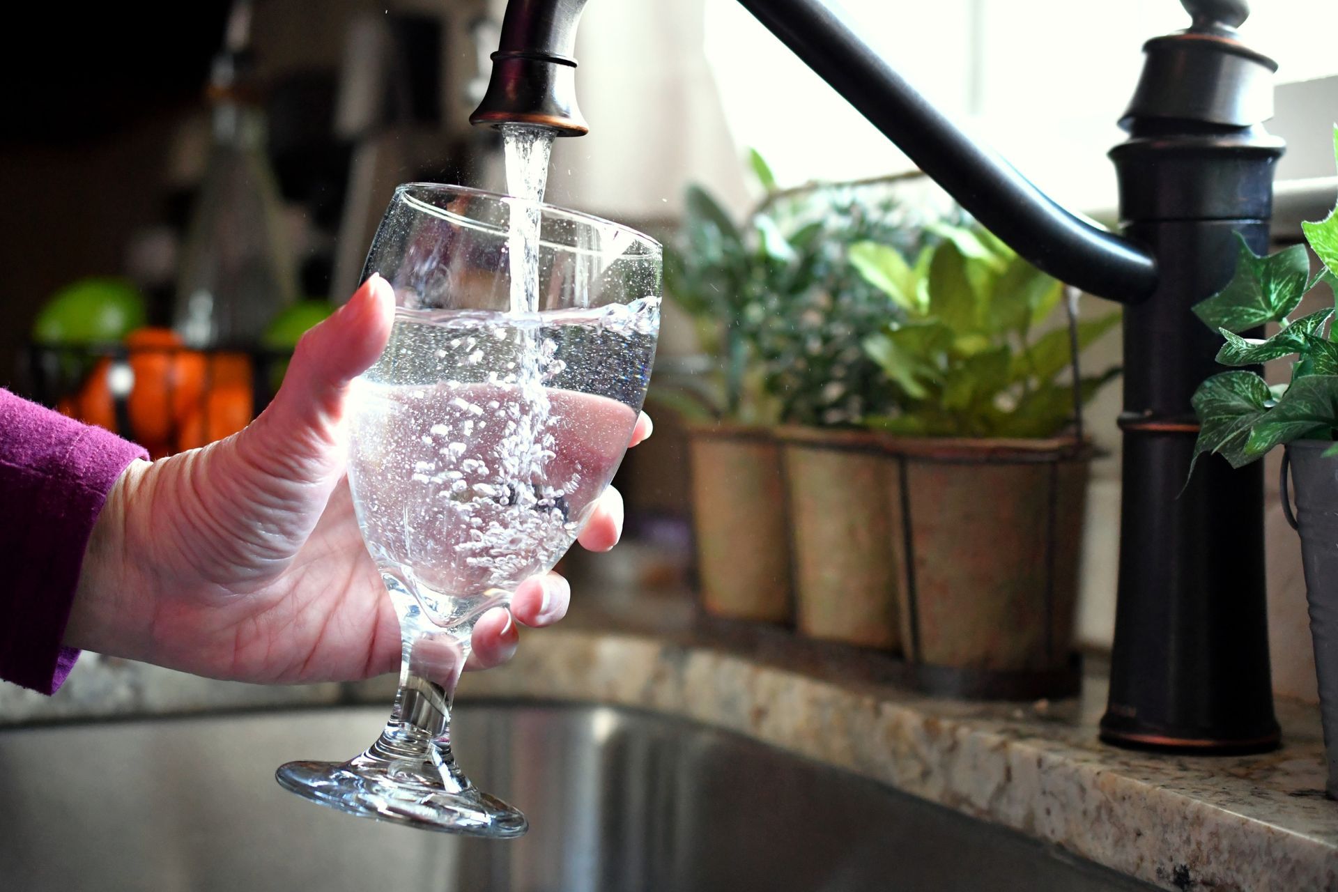 A person is pouring water into a wine glass from a faucet