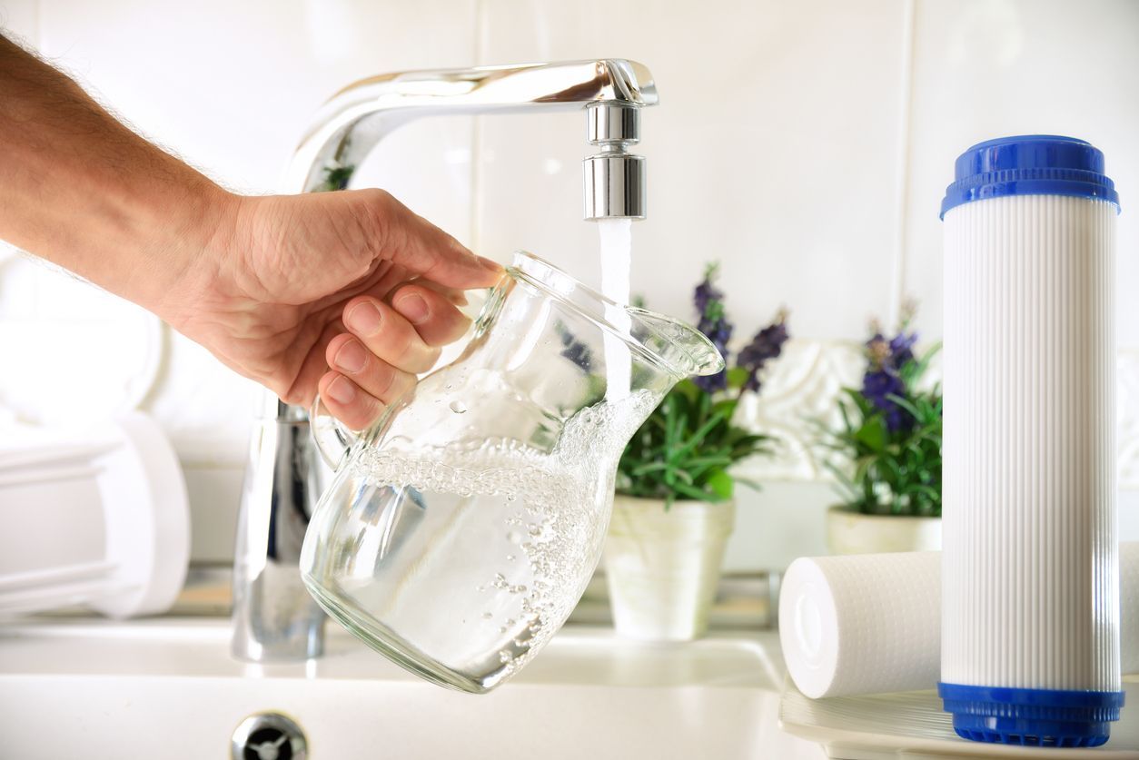 A person is pouring water into a glass from a faucet of filtered water