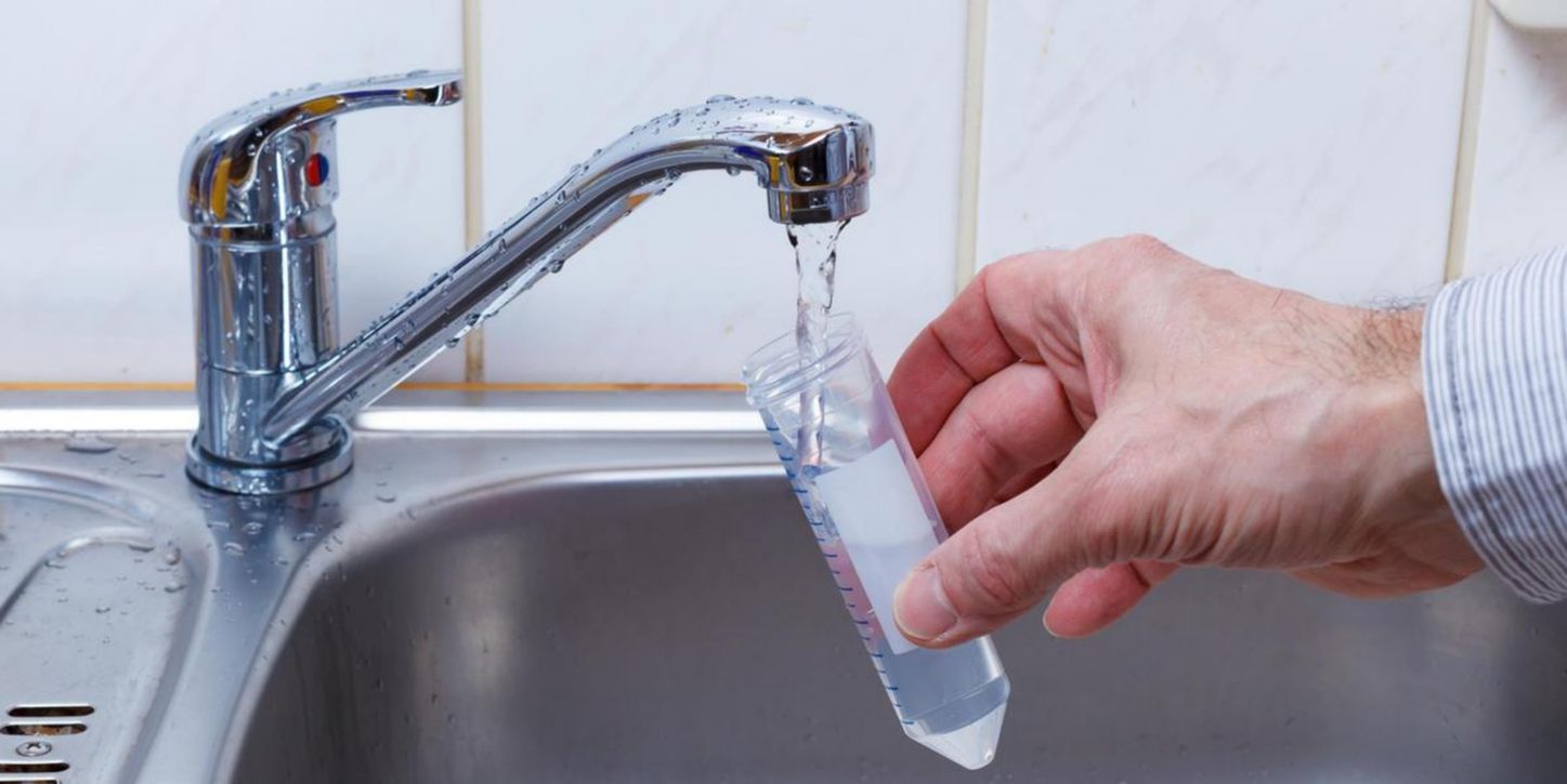 A person is pouring water into a test tube in a sink.