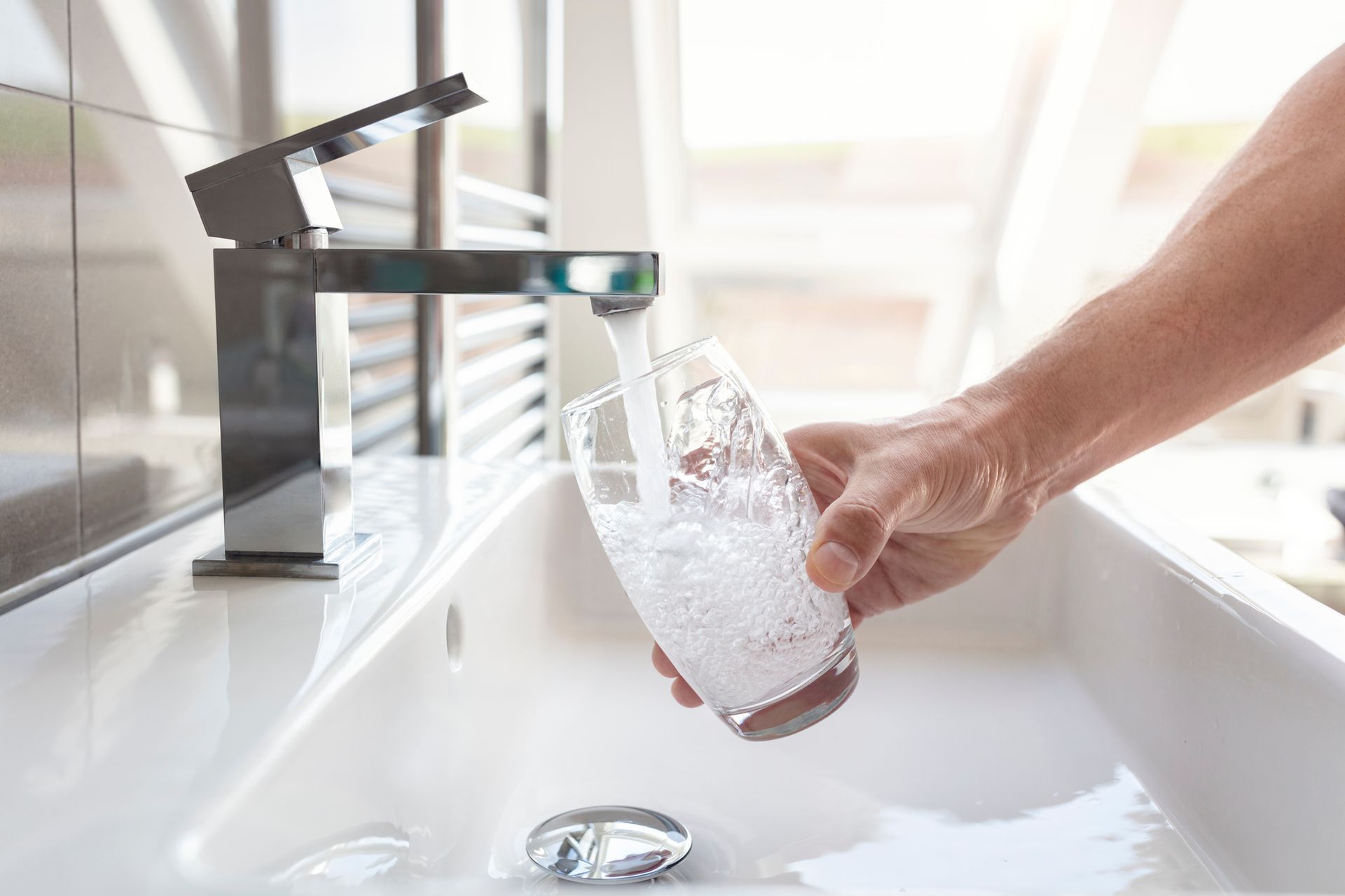 A person is pouring water into a glass from a faucet.