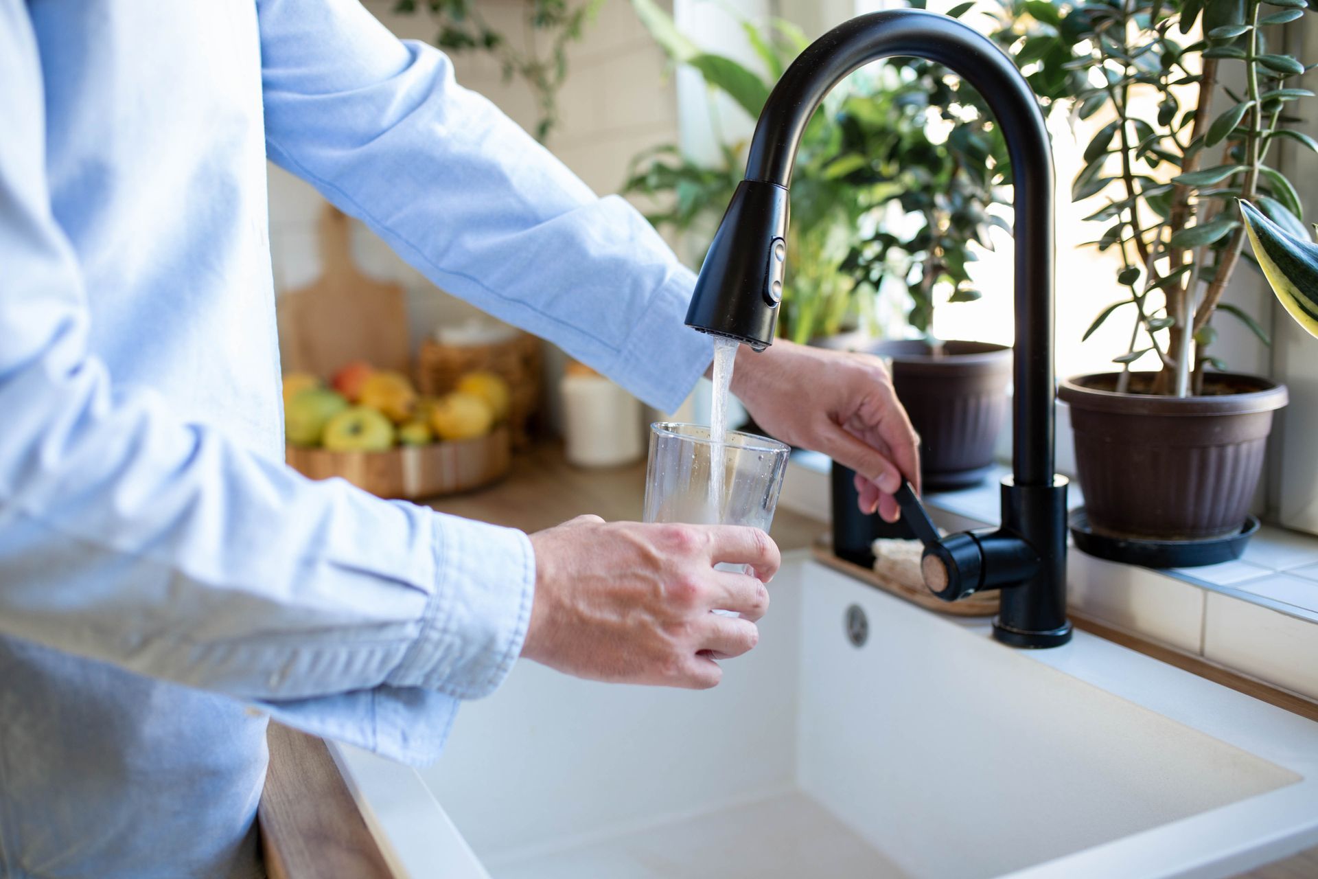 Person filling a glass with water from a black faucet in a kitchen sink.
