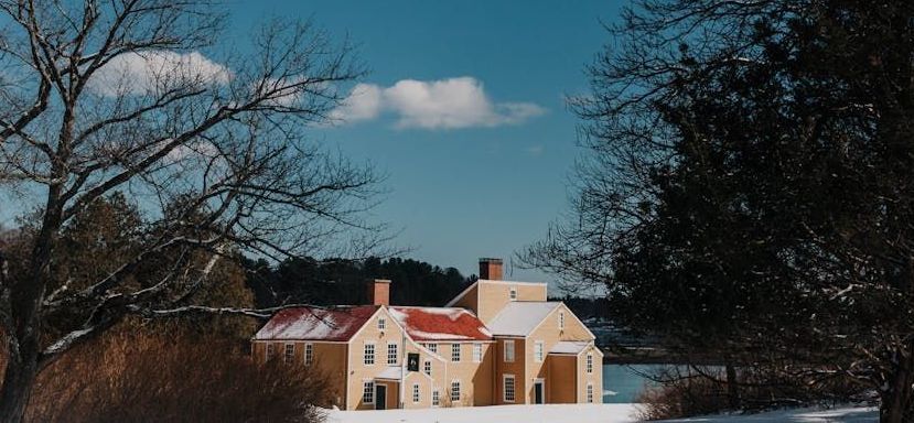 A large house with a red roof is surrounded by snow and trees.