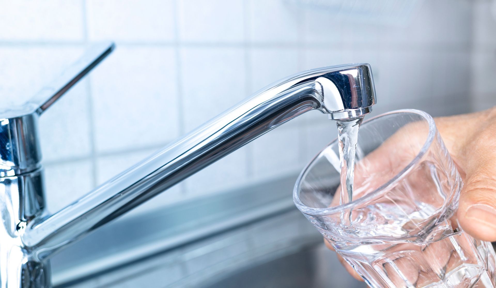 A person is pouring water into a glass from a faucet.