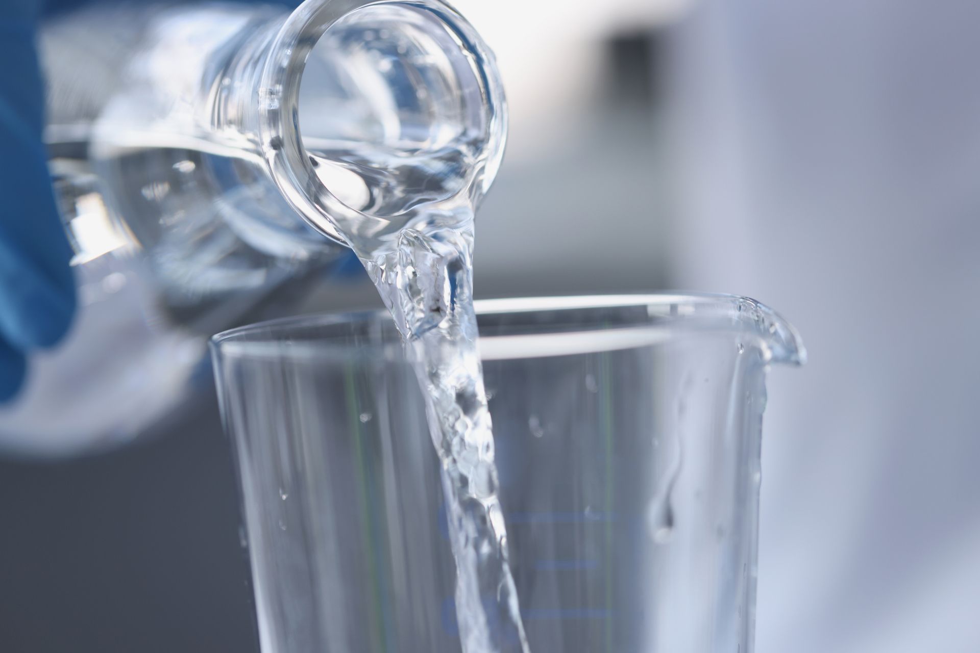 Clear liquid being poured from a glass container into a measuring beaker.