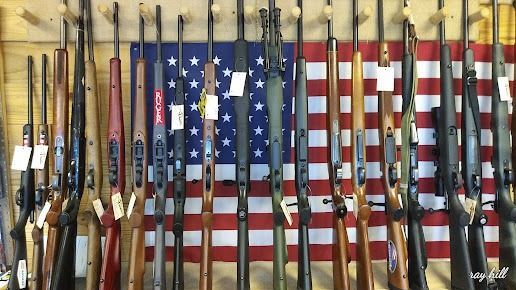 Boxes of model toy guns and accessories on a table, including several black and orange rifles.