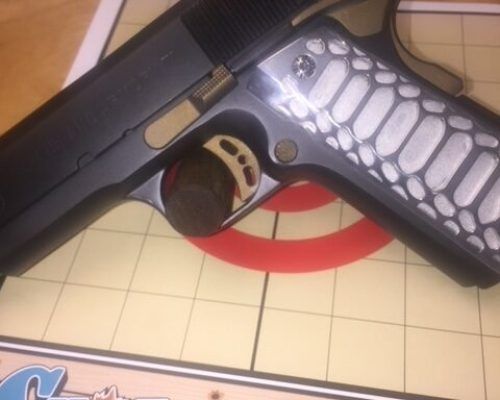 Black handgun with a silver slide and grip lies on a patterned mat.