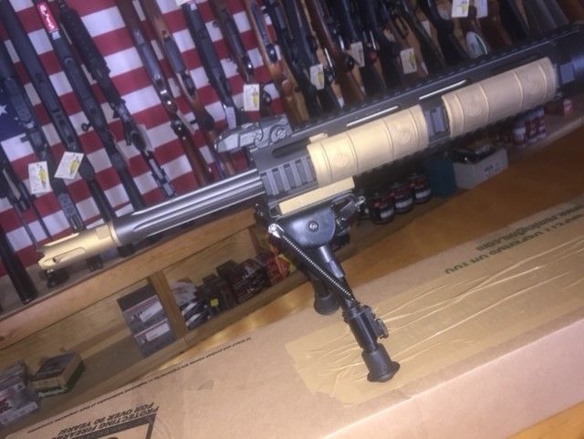 Rifle with scope and bipod resting on cardboard in a store aisle with shelves of fishing rods behind it