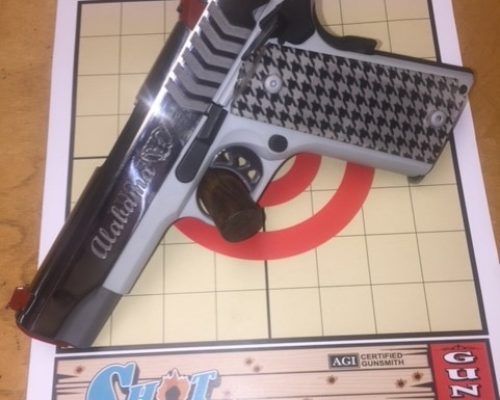 Silver-and-black handgun with checkered grip and black holster on a grid-patterned surface.
