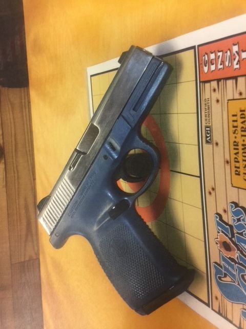 Black semi-automatic handgun on a wooden surface beside a board game box.