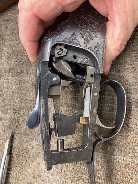 Close-up of a hand holding a carved metal firearm mechanism over a wooden surface