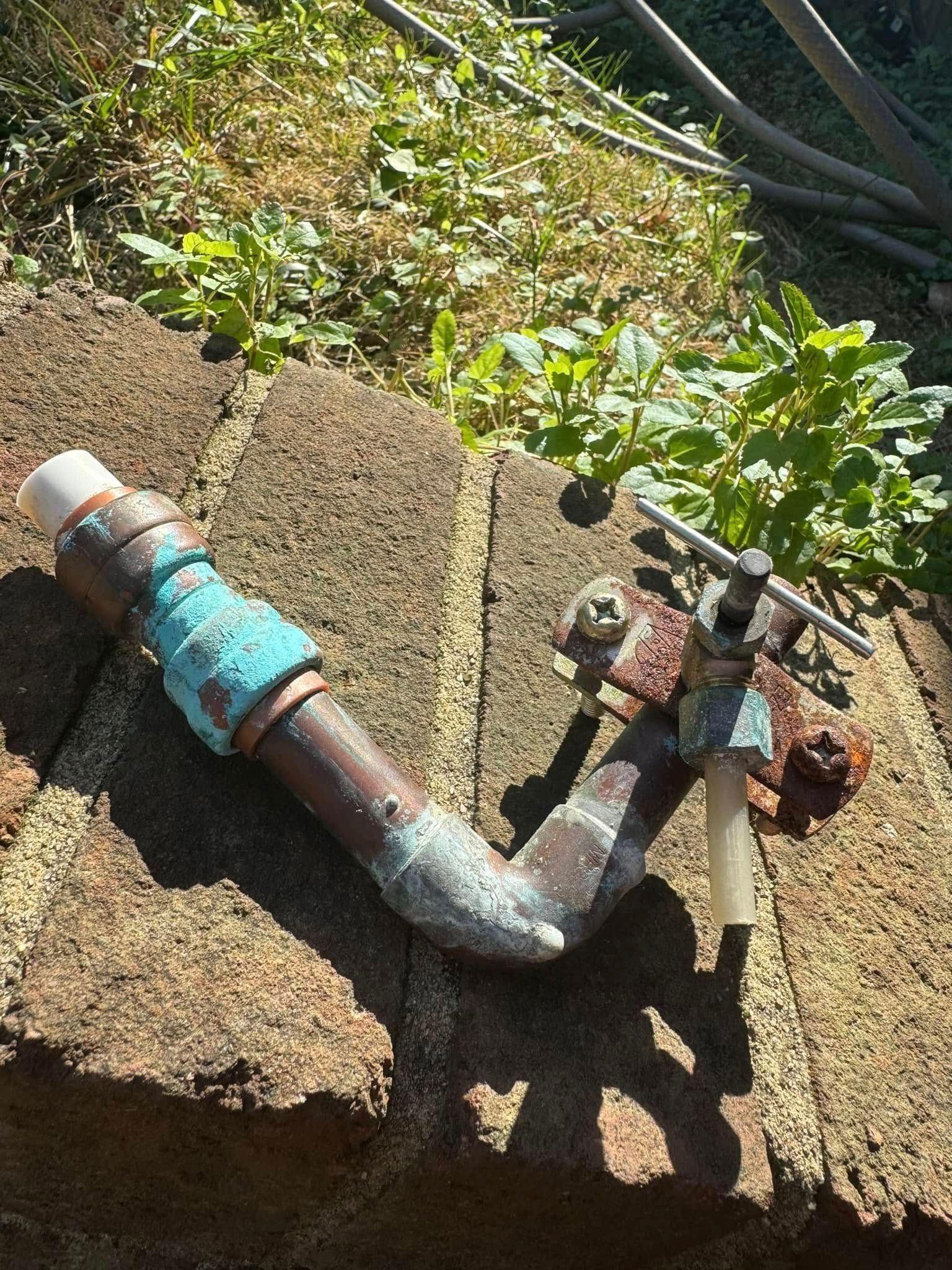 Old outdoor faucet and rusted pipe on a concrete block beside garden plants