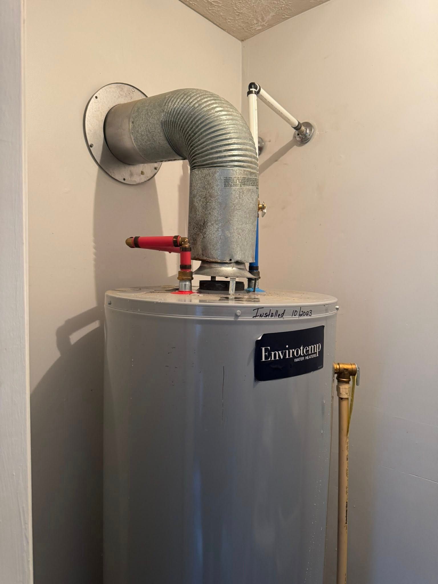 Water heater with a silver vent pipe and red shutoff valve in a utility closet.