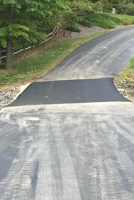 A person is spreading black paint on a concrete surface.
