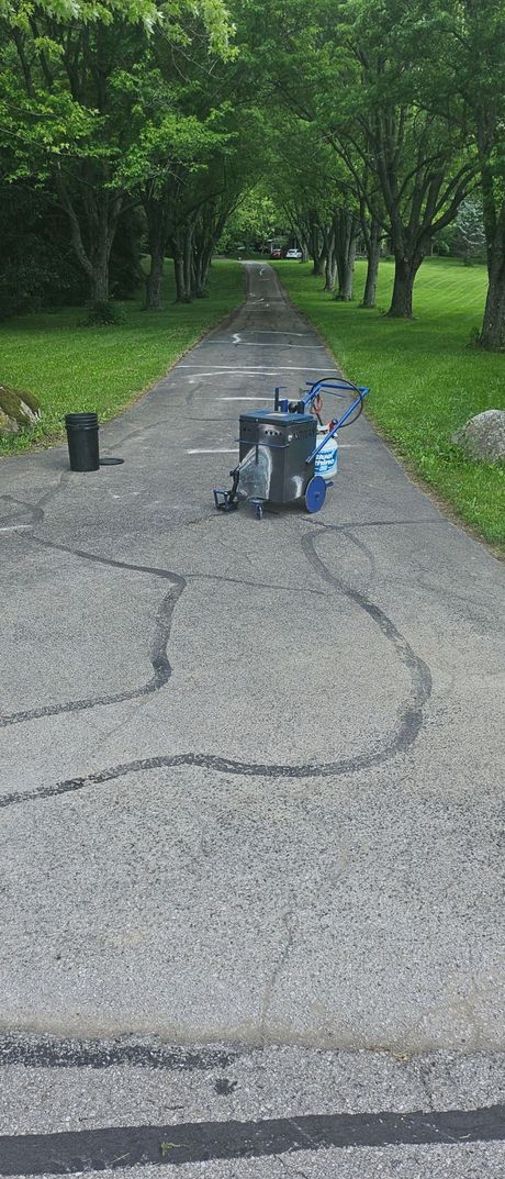 A man in orange pants is spraying asphalt on a road.
