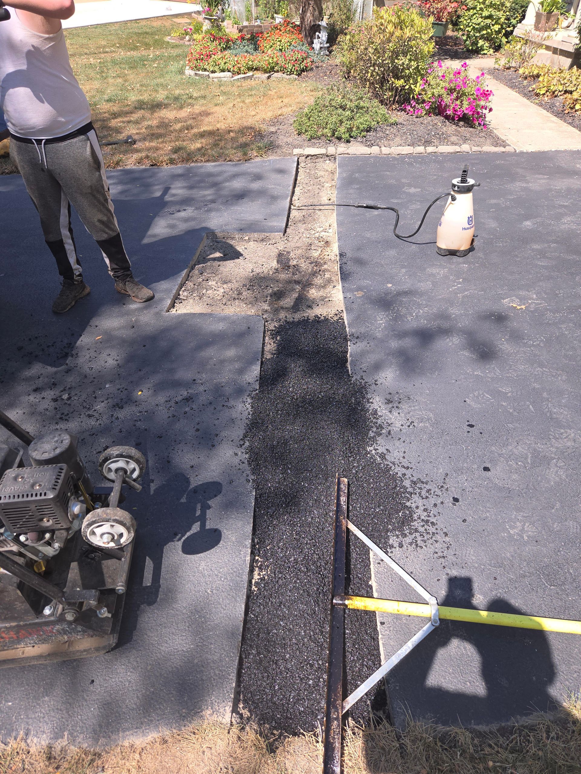 A man is standing next to a spray bottle in a driveway.